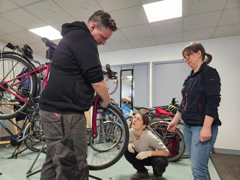 Photo de deux bénévoles pendant leur formation pour entretenir et réparer un vélo qui observent le formateur.