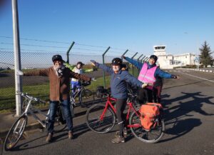 Quelques cyclistes mimant un avion avec les bras tendus devant l'aérodrome de Toussus le Noble