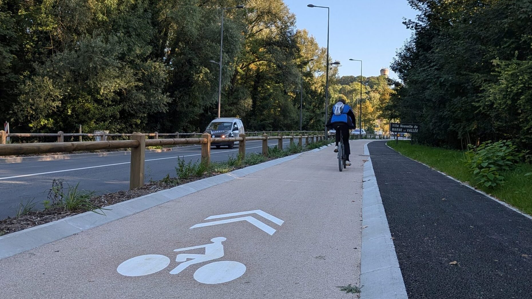 Piste cyclable de couleur ocre avec un picrogramme vélo et un double chevron. A quelques mètres, un cycliste s'éloigne sur la piste.