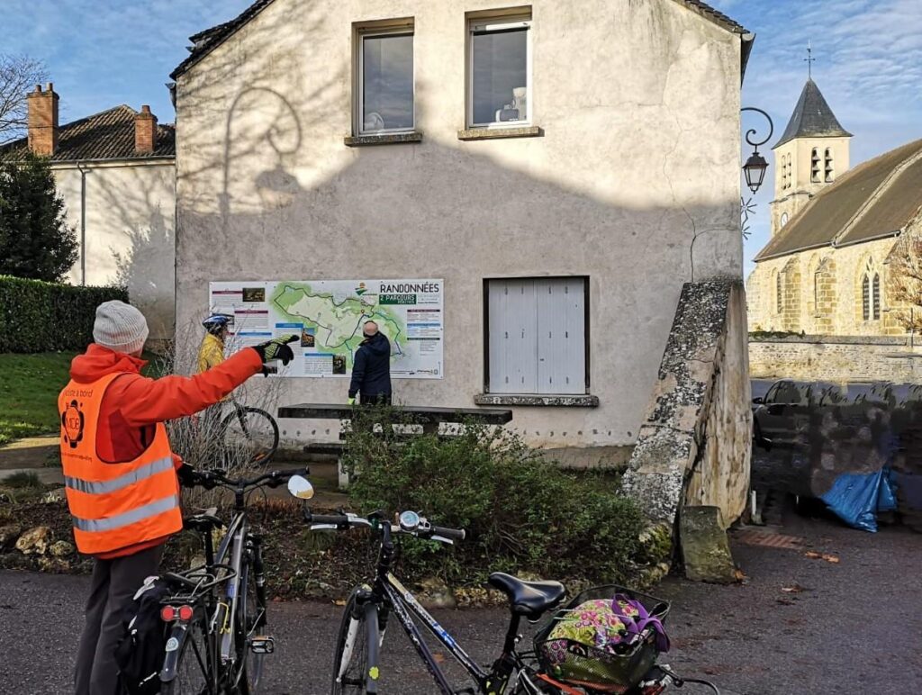 Adhérent et vélos pointant un panneau décrivant un circuit de randonnée